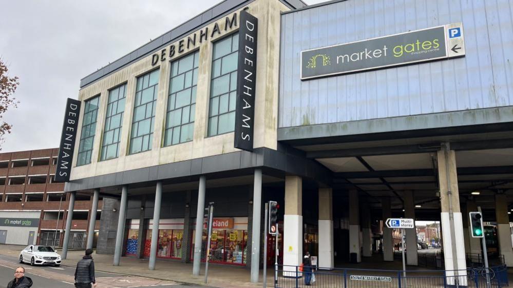 Market Gates shopping centre extension featuring glazed windows above a discount supermarket with concrete pillars holding up the structure. To the left is the adjacent multi storey car park