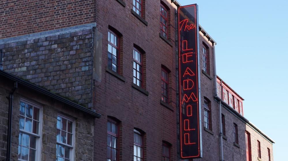 The façade of the Leadmill nightclub in Sheffield. It has a vertical sign spelling the venue name in capital letters lined with neon red lighting.