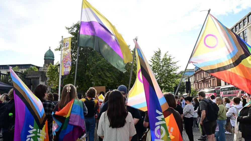 People standing outside City Hall. People are holding rainbow flags.