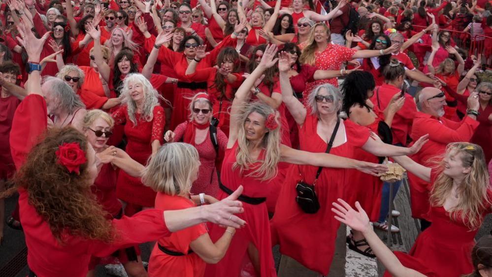 A group of people in red dresses dance with their arms in the air.