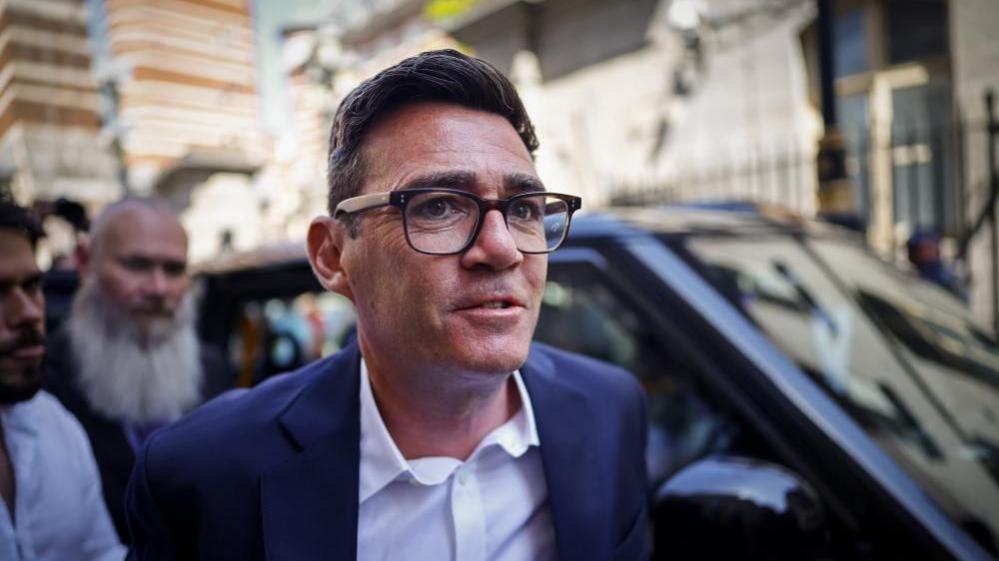 Image shows Andy Burnham wearing black-rimmed glasses and a blue suit, arriving at the Houses of Parliament in Westminster, London, Britain, on 22 June 2026