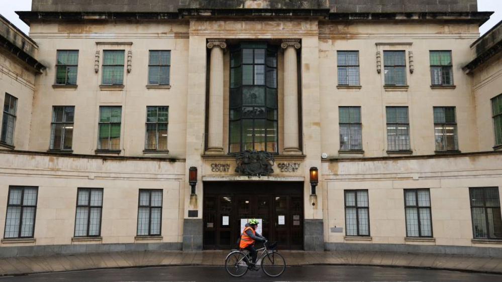 Oxford Crown Court, a large building made of light brown Cotswold stone. A cyclist is passing by.
