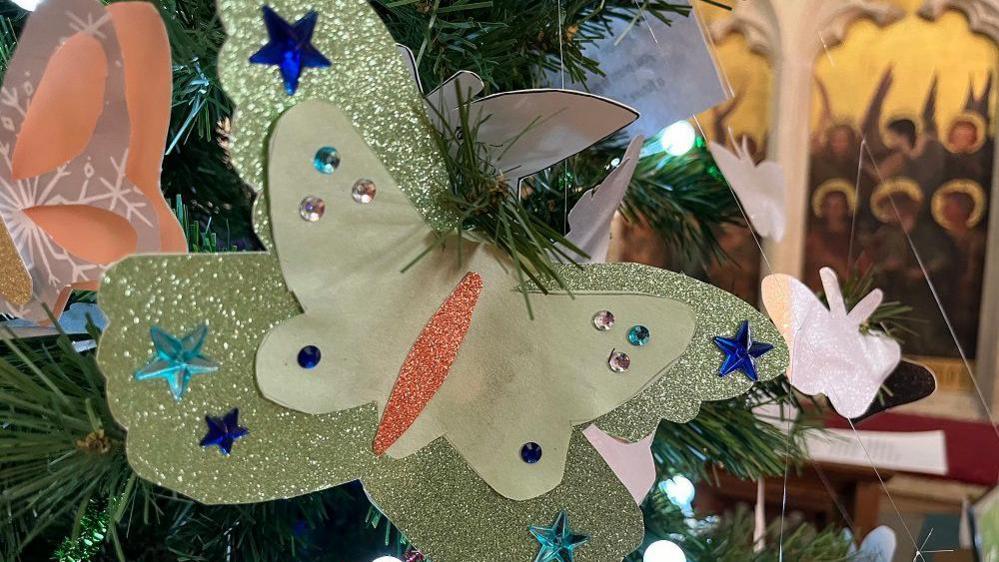 A glittery cardboard butterfly on a tree branch with others behind it 