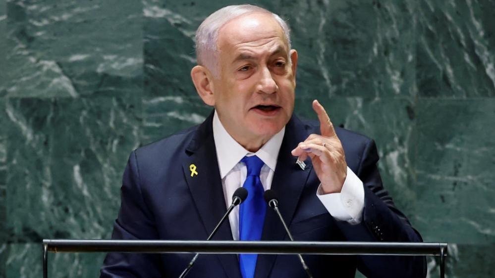 Israel's Prime Minister Benjamin Netanyahu addresses the UN General Assembly in New York. He is wearing a blue suit and holding up a finger as he speaks.