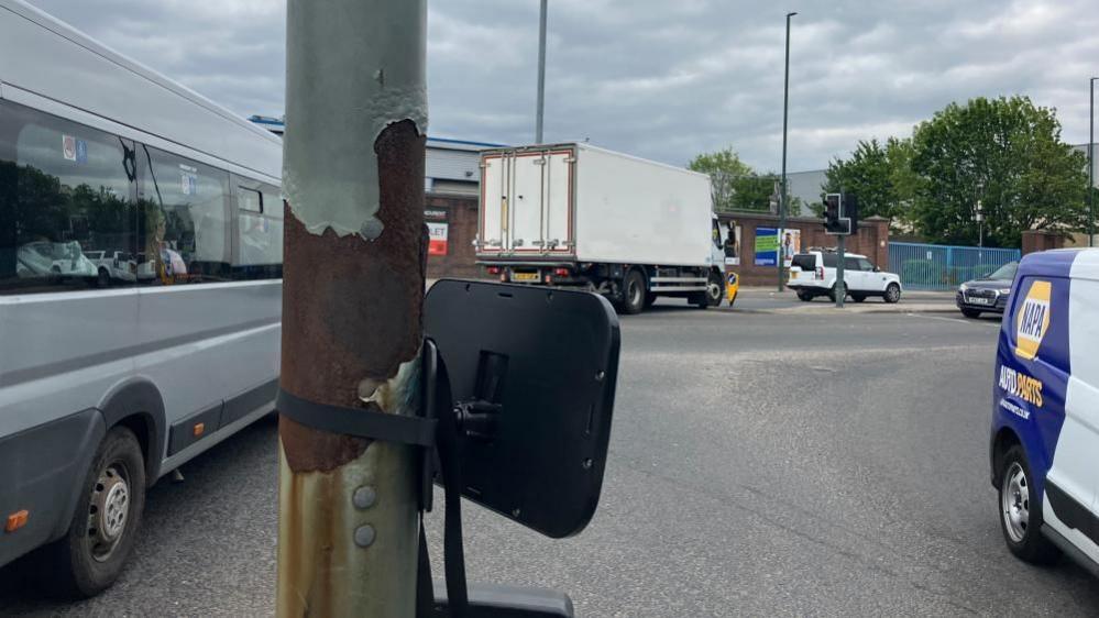 An image of the mirror strapped to a lamppost on the junction of Lady Bay Bridge and Meadows Lane. There are cars on either side of the island.