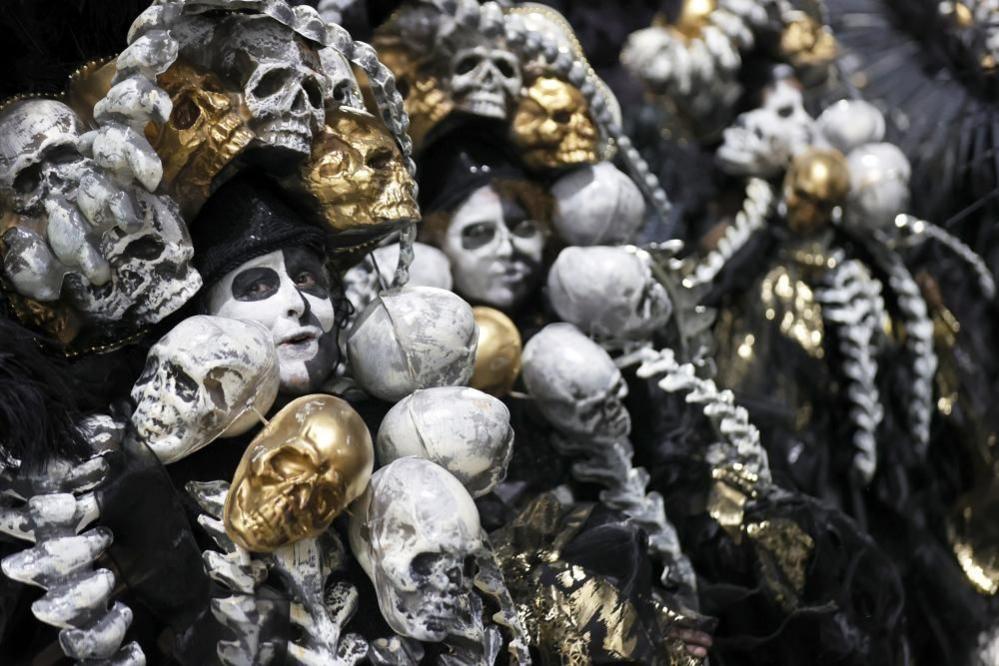 Members of the Imperatriz samba school, their faces painted in white and black paint, are surrounded by plastic skulls, some painted white, others gold 