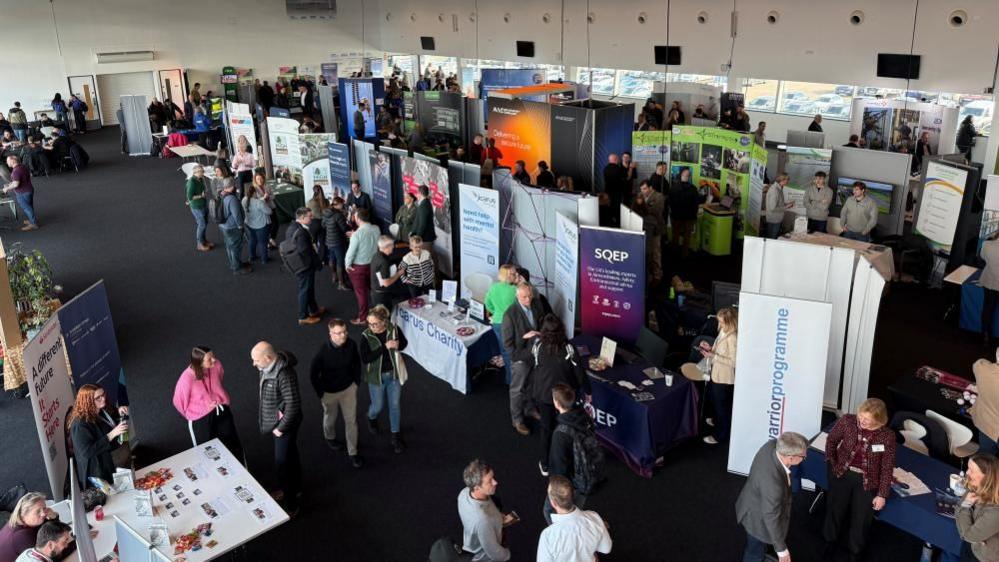 Lots of people wandering around a hall with exhibitions set up