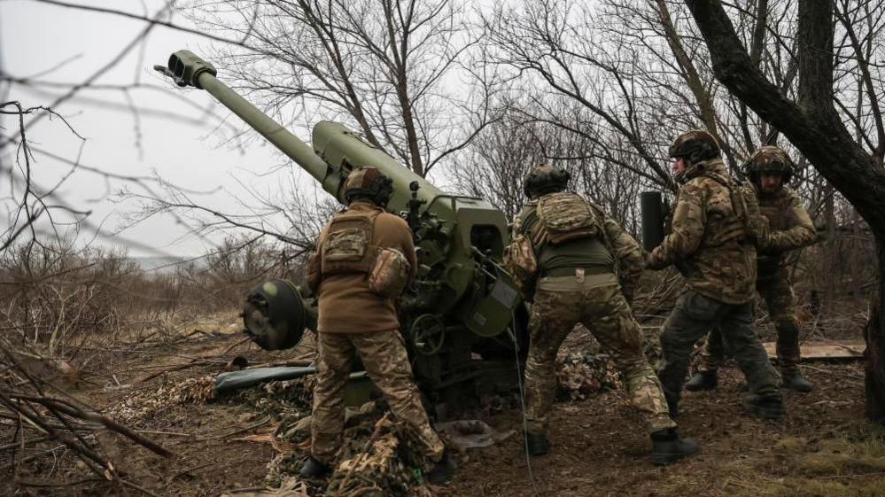 Ukrainian soldiers in brown camouflage fire a howitzer into the distance