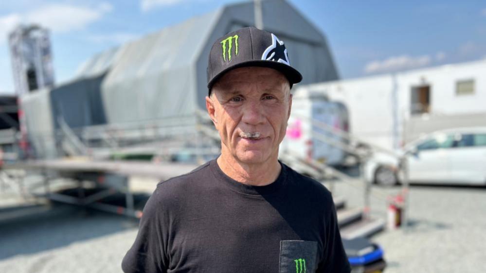 Randy Mamola wearing a black cap and a black T-shirt in the Silverstone paddock