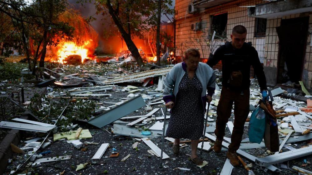 A woman receives assistance as she leaves the apartment building hit during Russian missile and drone strikes in Kyiv, Ukraine early on Thursday