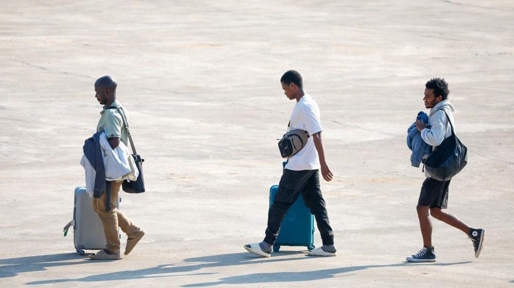 Three people released from scam centres walk across a tarmac