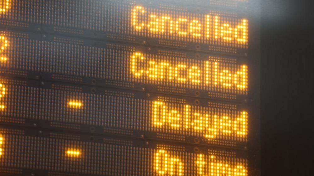 Close up image of a display board in a train station. The board says cancelled, cancelled, delayed and on time.