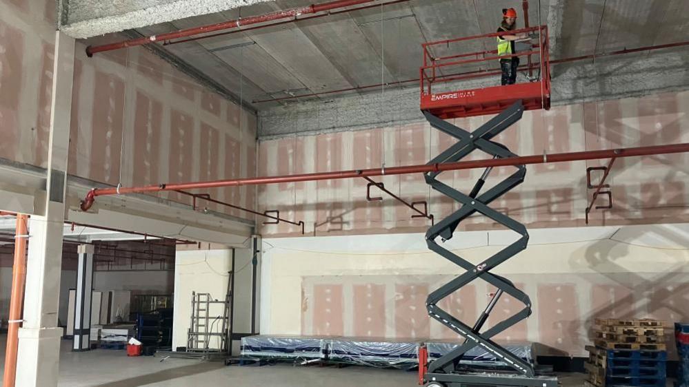 A man on mobile elevated work platform looking down at an empty shop unit which has been stripped back and is under construction. 