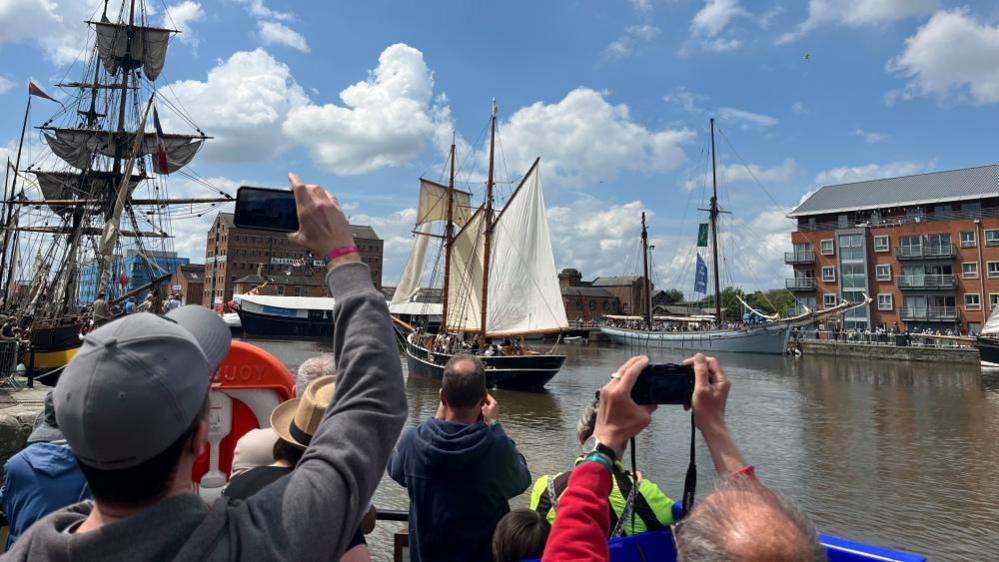 People taking photos of tall ships at Gloucester Docks. The picture is taken on a sunny day with light cloud