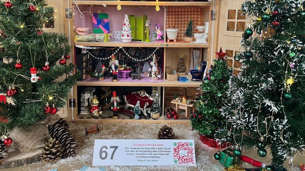 An open doll's house with a Christmas theme with two smaller Christmas trees in front