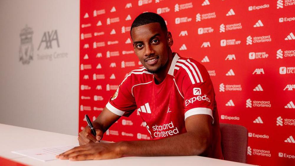 Alexander Isak signs for Liverpool while wearing his new team's red shirt