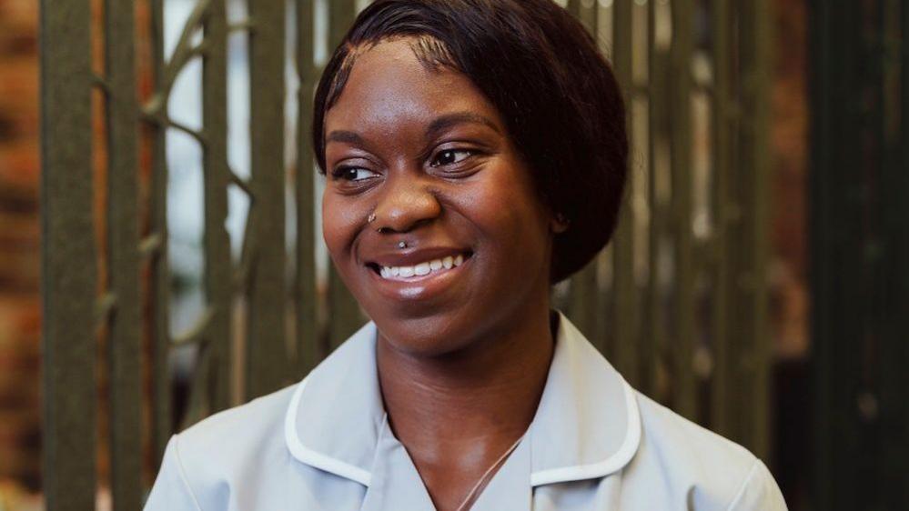 Asia Mason smiling at her workplace, looking slightly to the right of the camera and wearing her scrubs.
