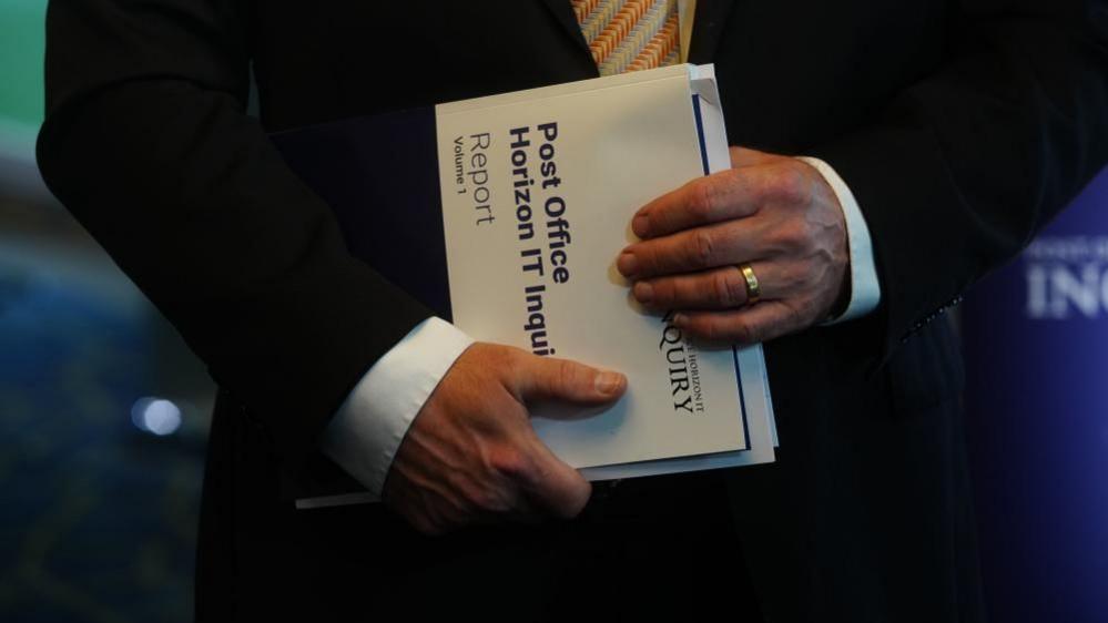 A man holds a copy of the Post Office Inquiry report