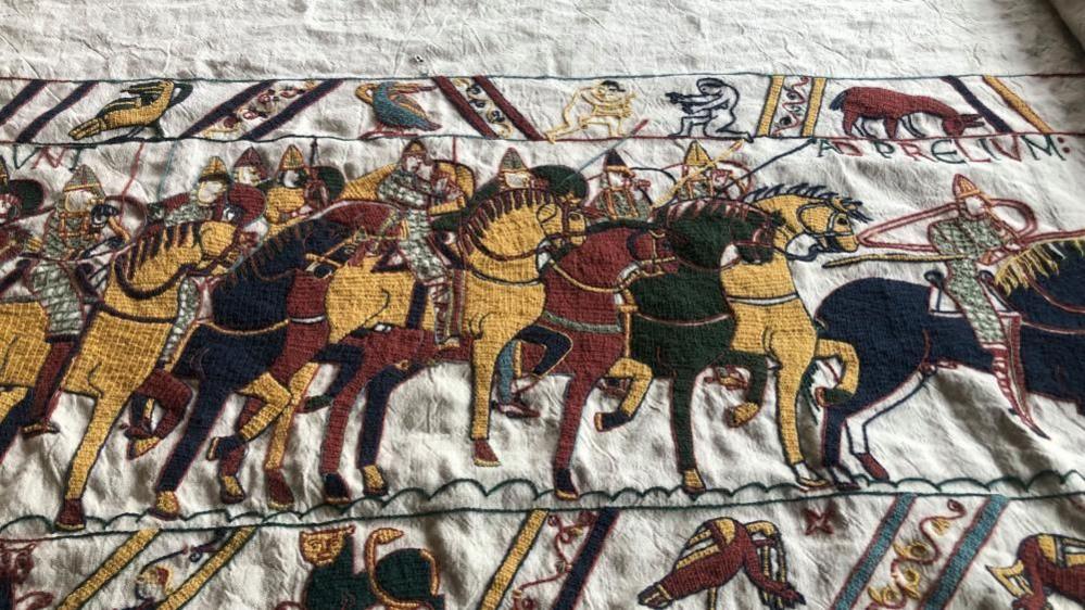 Detail of replica tapestry showing embroidered battalion of horses behind William the Conqueror, in chainmail