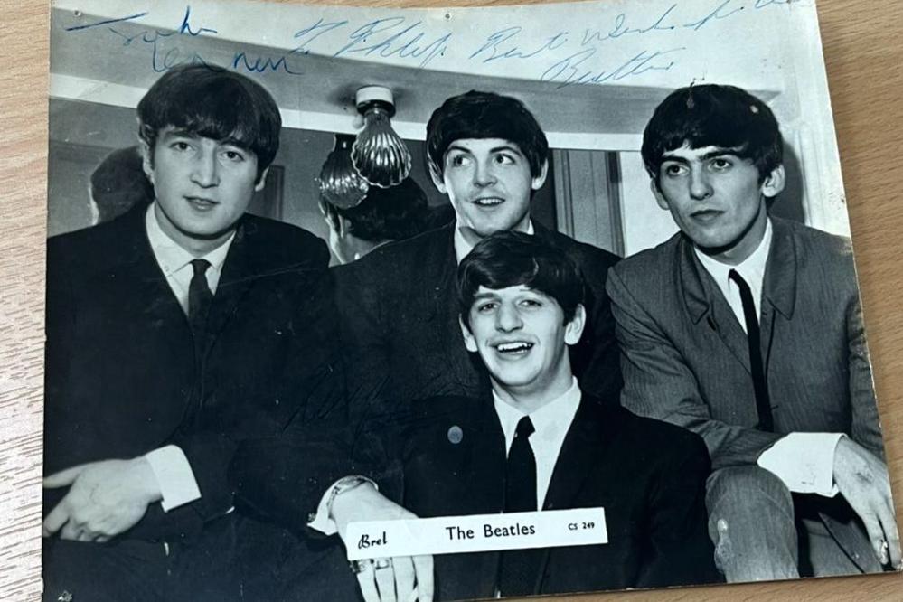 A close-up image of the signed black-and-white photo of the Beatles. John Lennon, Paul McCartney, George Harrison and Ringo Starr are wearing suits with white shirts and black ties
