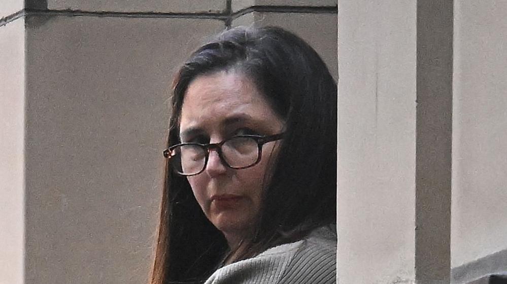 Erin Patterson, with long brown hair and wearing dark glasses, is looking over her left shoulder to the right