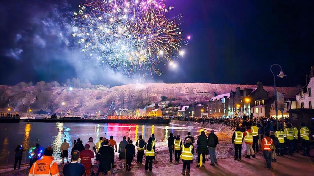 Fireworks are set off as people stand by the weather watching them.