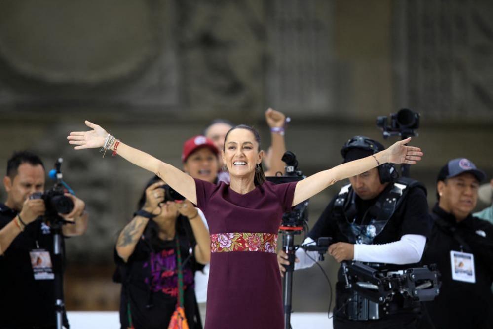 Mexican presidential candidate Claudia Sheinbaum stands with her arms outstretched on stage at a campaign event. 