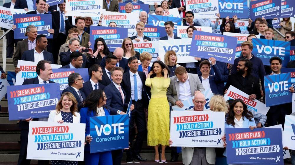 Rishi Sunak in dark suit surrounded by supporters with blue placards