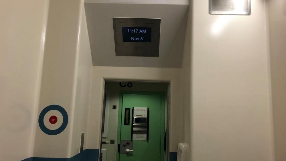 A view of a green prison door looking out from with in the cell and above which is a TV screen. There is also a target on the walls. The picture is to illustrate how in-cell technology is being used inside police cells.  