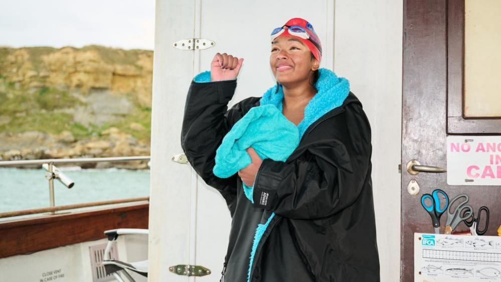 Prisha Tapre is a black and blue DryRobe, standing on a boat and holding a towel