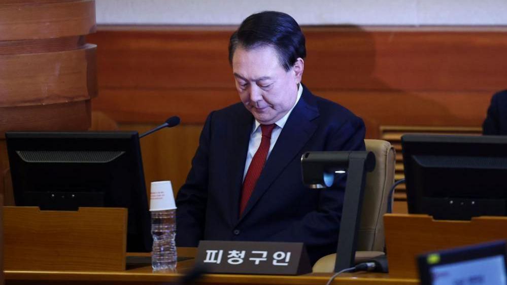 South Korean Yoon Suk Yeol looking downwards while sitting in the dock in a courtroom