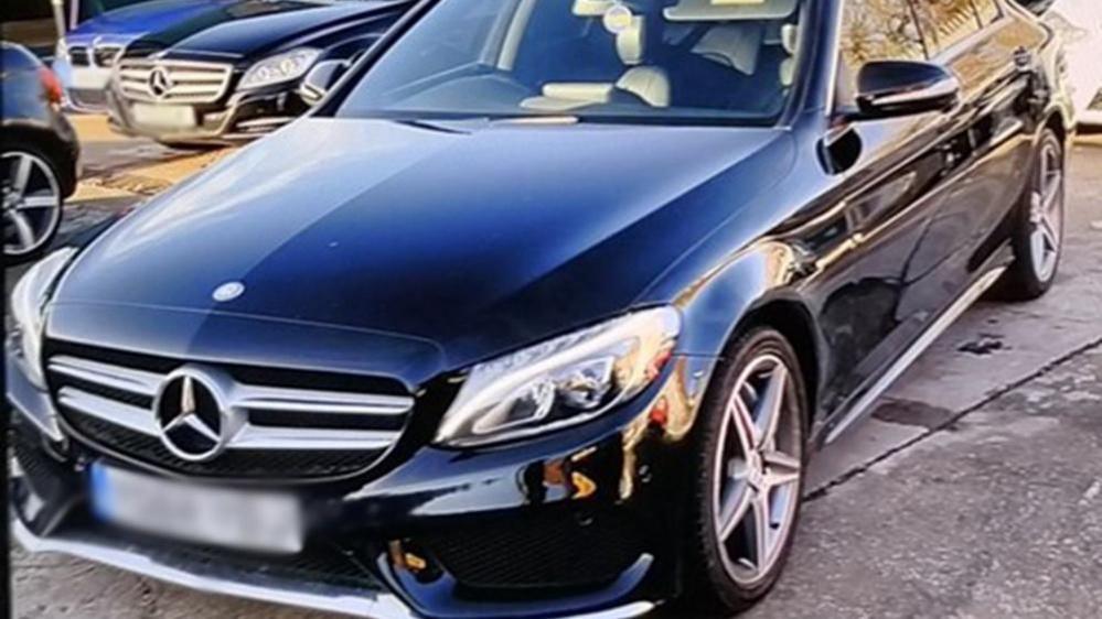 A black Mercedes Benz car parked in a concrete carpark.