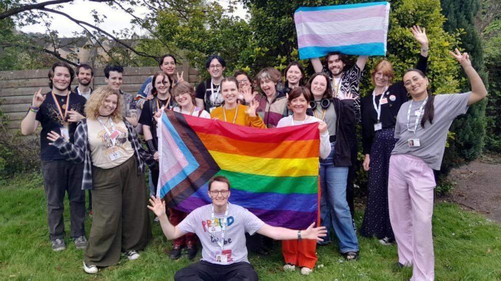 Users of Off the Record mental health services in Bath and North East Somerset. They are holding up a large pride flag and also a trans rights flag