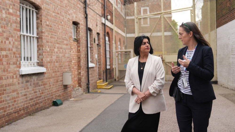 Justice Secretary Shabana Mahmood touring a prison with HMP Bedford Governor Sarah Bott. They are seen talking in a prison yard. 