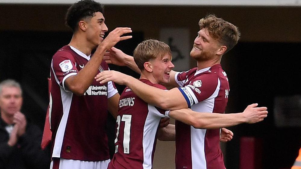 Jack Perkins is embraced by two Northampton team-mates after scoring in their game against Mansfield Town