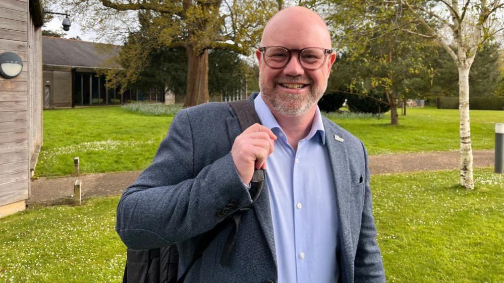 Gerald McCleave wearing a suit, open shirt and carrying a bag