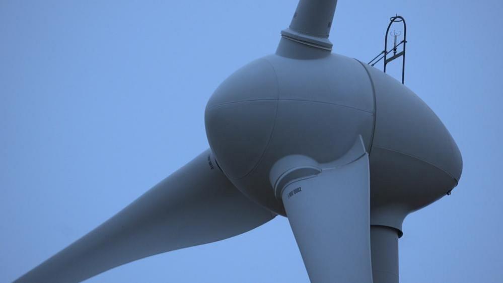 A close-up of the top of a wind turbine seen against a blue sky