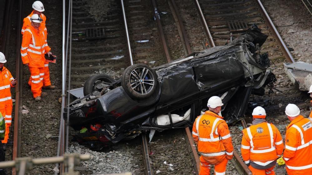 Engineers examine the wreck of a car which crashed on to the main Chat Moss rail line at Salford, Greater Manchester