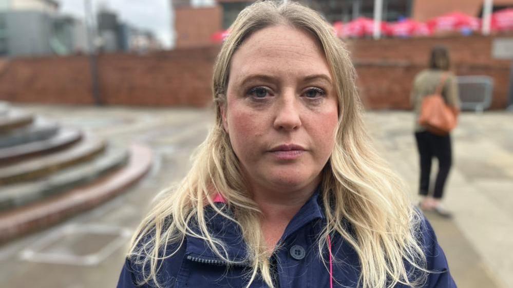 Kirby Hoyle stands outside the housing conference. She has long blonde hair and is wearing a blue jacket.
