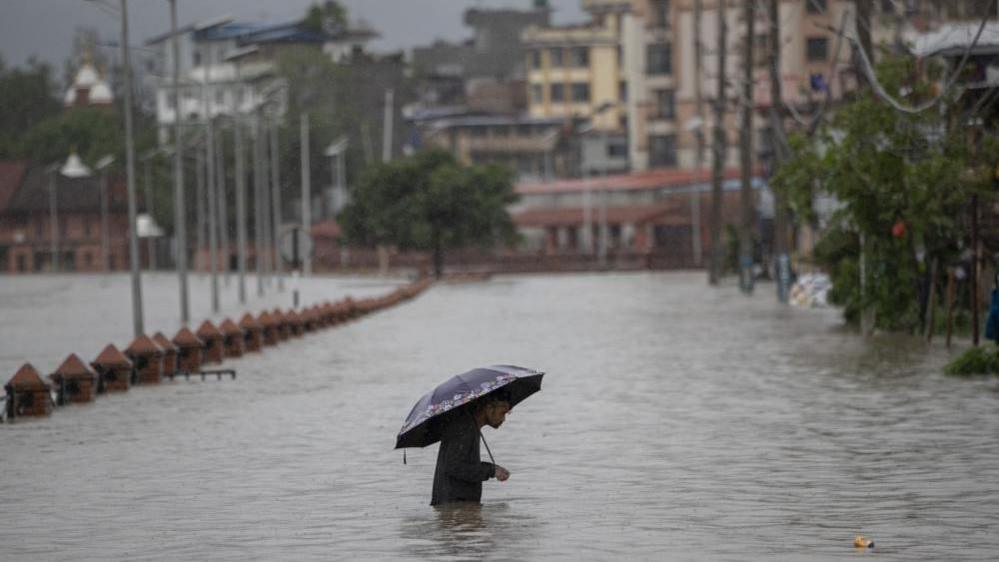 A person wades through a flooded street caused by the swollen Bagmati River after torrential rains in Kathmandu, Nepal, 6 July 2024. 