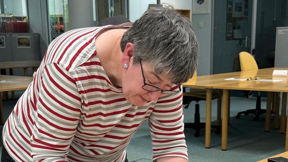 Ruth Butler wearing a striped t-shirt looking down at a document in the history centre