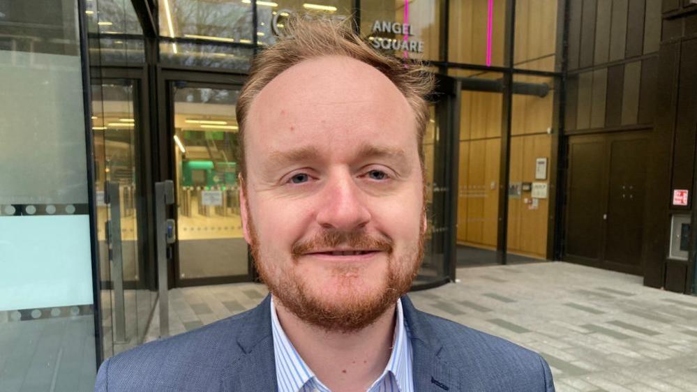 Adam Brown with short brown hair and beard standing in front of council offices