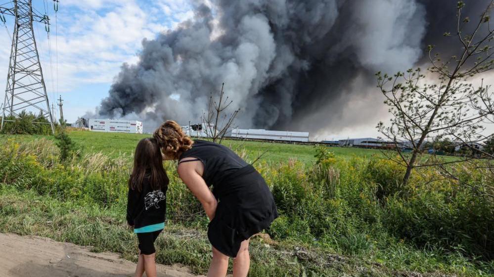 People watch as smoke rises above a Wildberries facility following a reported Ukrainian drone strike at the Koledino Industrial Park near Podolsk in Russia on 16 August.