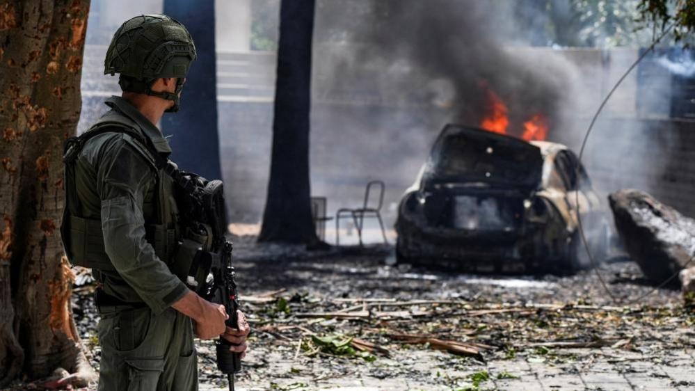 A soldier in Kiryat Shmona looks at a burning car at the impact site of a rocket that was fired towards Israel from Lebanon (05/05/24)