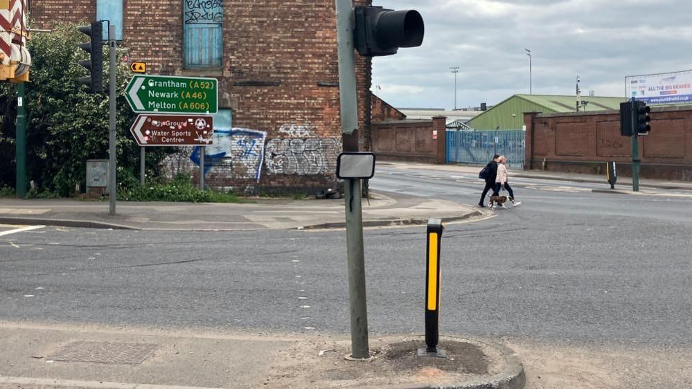 A convex mirror strapped to a lamppost on a traffic island at the junction of Lady Bay Bridge and Meadow Lane. Cars can be seen in the reflection of the mirror.