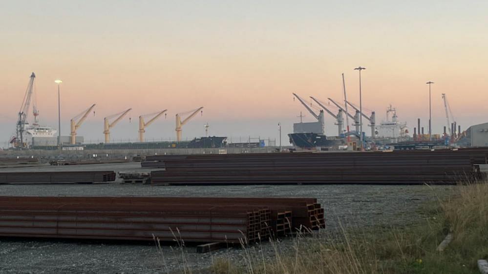 MV Ruby on the left with MV Zimrida on the right. Steel is stacked up in the foreground. The sky has a pink hazy sunset.