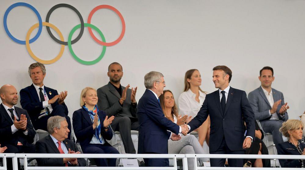 A smiling French President Emmanuel Macron (R) shakes hands with IOC president Thomas Bach as they take their seats in the Trocadero