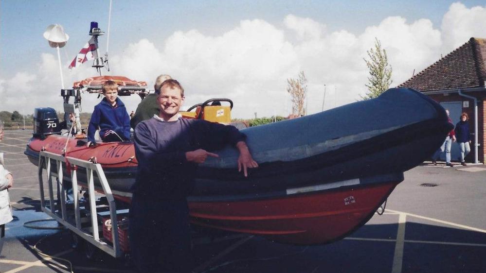 Nick Hayward standing smiling at the camera next to a lifeboat.