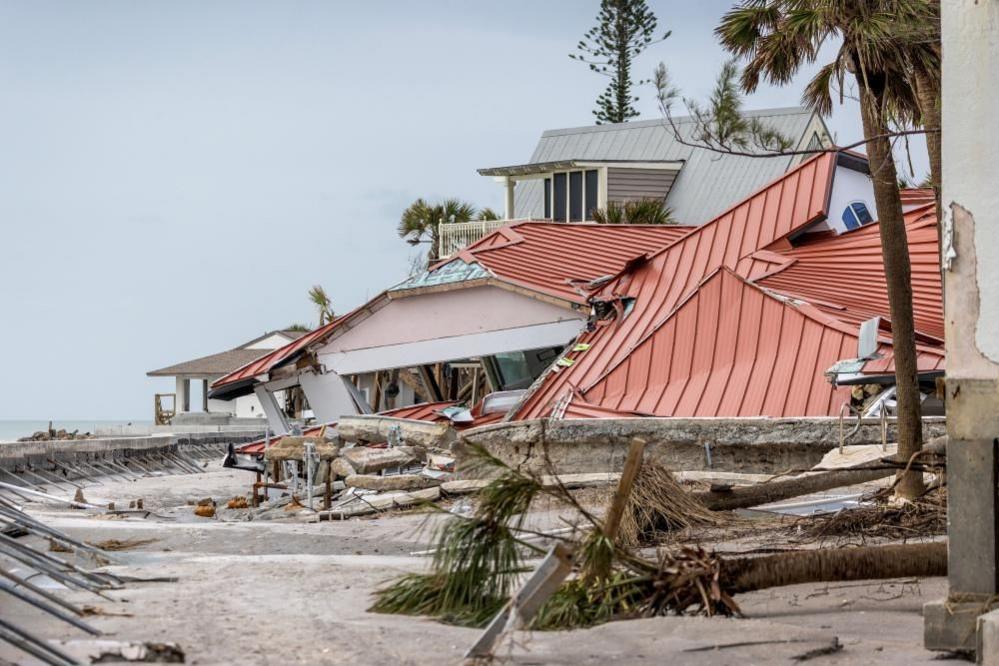 A battered house in the aftermath of a hurricane, there are fallen trees in the foreground. 