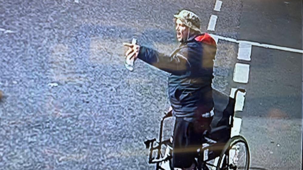 Michael McQueen, standing near his wheelchair, in the junction of St Peter's Road and King Street in Great Yarmouth. He is holding a bottle of beer in his right hand. McQueen has one leg, is wearing a camouflage hat, a blue jacket with red hood lining.